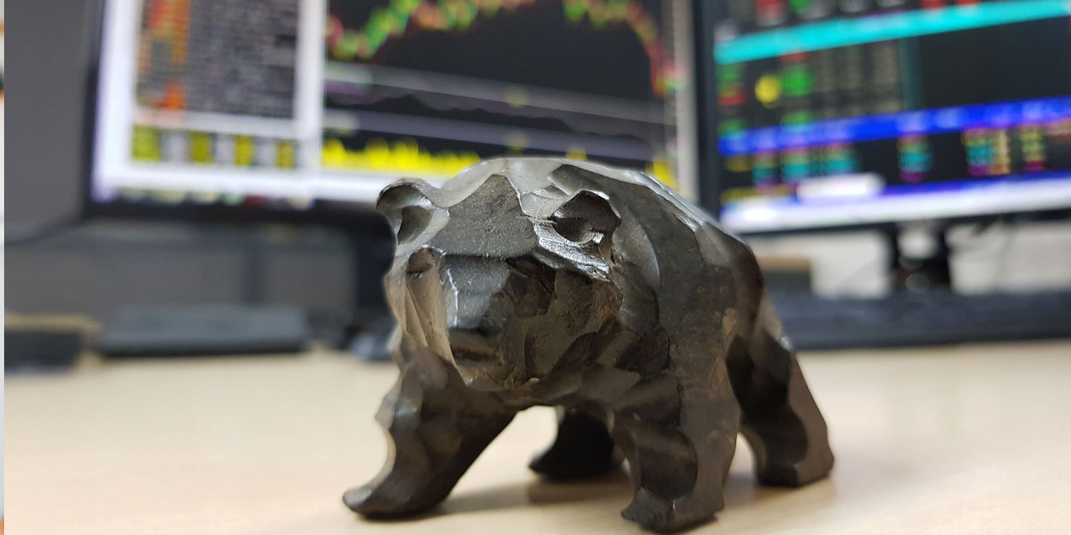Miniature wooden bear on a desk in front of stock monitors